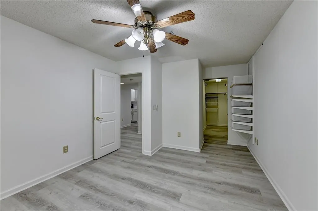 Unfurnished bedroom with light wood finished floors, a textured ceiling, a spacious closet, and ceiling fan
