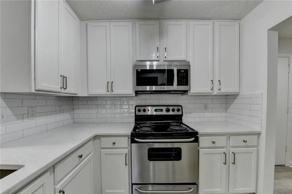 Kitchen featuring stainless steel appliances, white cabinets, light stone countertops, tasteful backsplash, and a textured ceiling