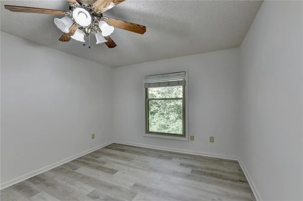 Empty room with a textured ceiling, light wood-type flooring, and ceiling fan