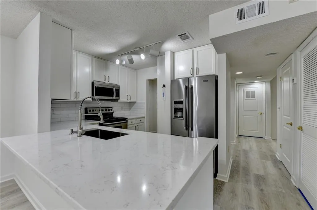 Kitchen with decorative backsplash, white cabinets, appliances with stainless steel finishes, light wood-style flooring, and a textured ceiling