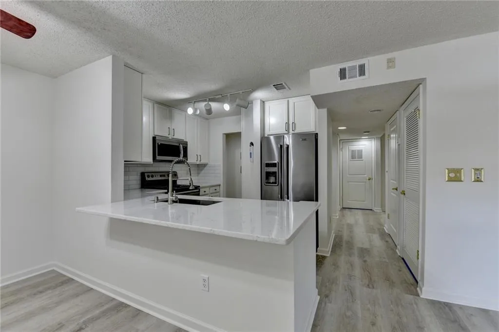 Kitchen featuring decorative backsplash, white cabinetry, appliances with stainless steel finishes, light wood-type flooring, and light stone countertops