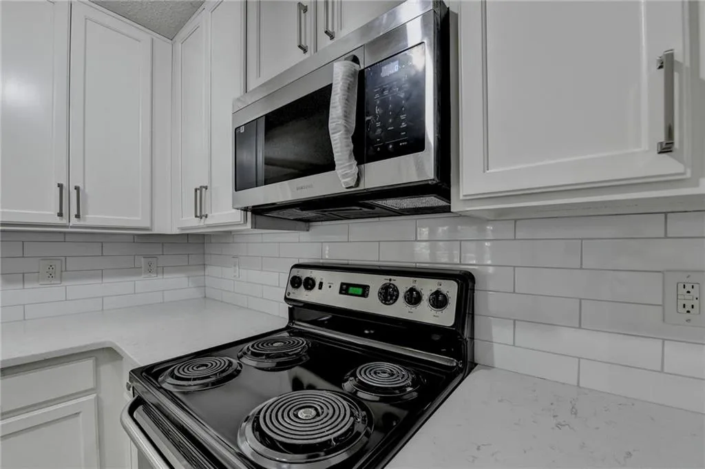 Kitchen featuring electric stove, white cabinets, stainless steel microwave, and backsplash