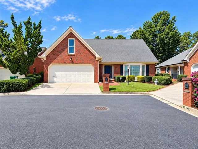 Brick exterior with an attached two-car garage, concrete driveway, and established landscaping