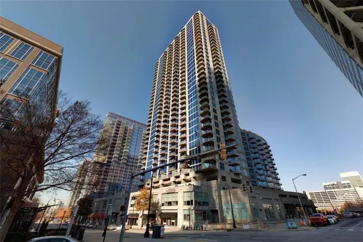 Contemporary high-rise building featuring a multi-story base, extensive glass facade, individual private balconies, and a distinctive rounded architectural element