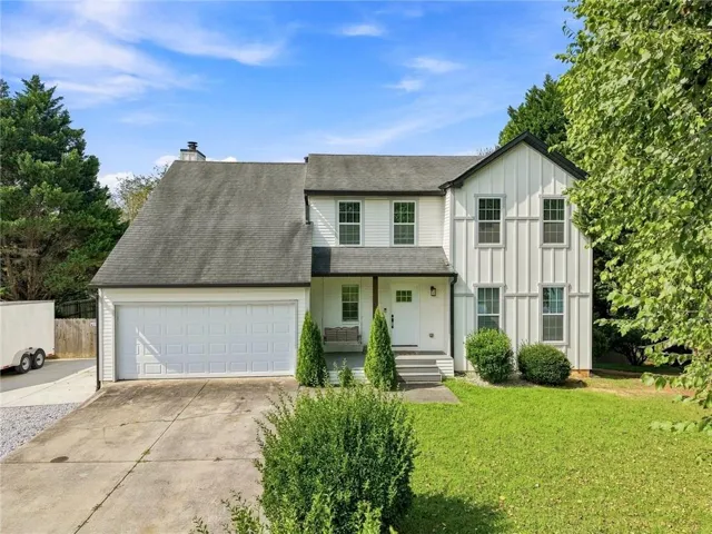 Modern Colonial two-story residence featuring a clean white exterior with black-trimmed windows, a prominent front-facing garage with paneled doors, and a gabled roofline with architectural detailing