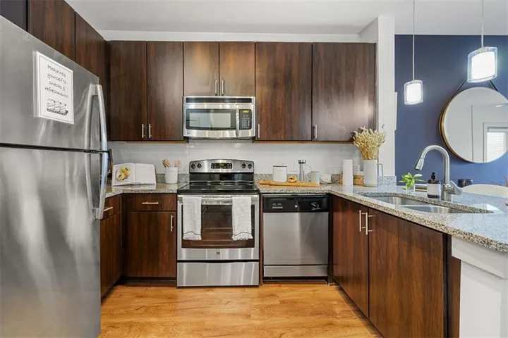 Kitchen featuring wood-finish cabinetry, stainless steel appliances, speckled stone countertops, and a white subway tile backsplash