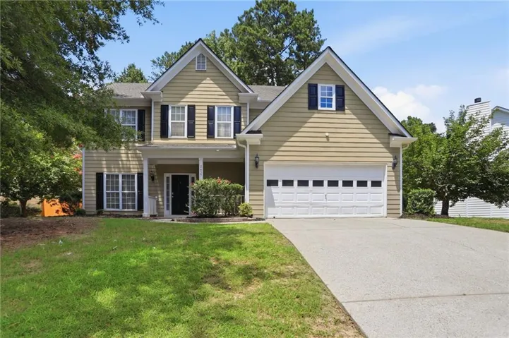 Two-story Colonial-style home featuring a tan vinyl siding exterior with contrasting dark blue shutters and multiple gabled rooflines