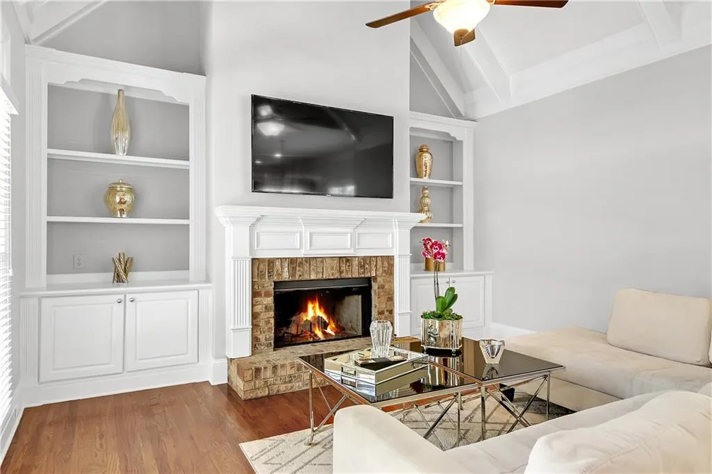 Living room with ceiling fan, wood-type flooring, a brick fireplace, built in features, and lofted ceiling