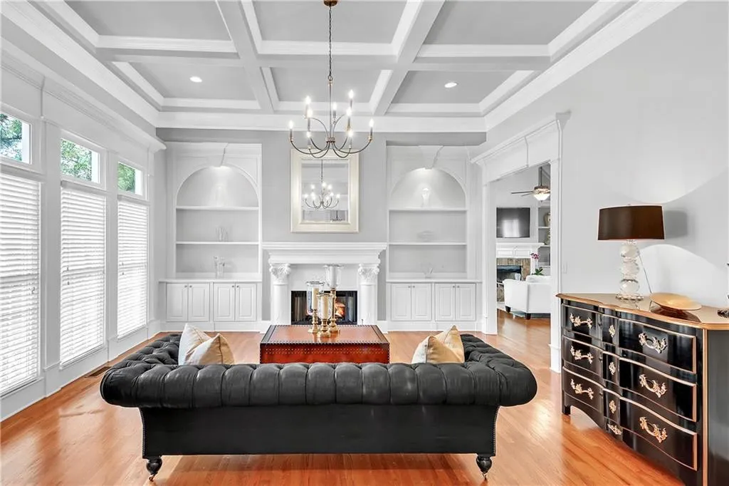 Living room featuring coffered ceiling, light hardwood / wood-style flooring, ceiling fan with notable chandelier, beam ceiling, and built in shelves
