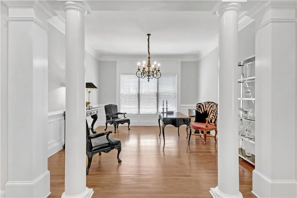 Living area with a notable chandelier, ornamental molding, wood-type flooring, and decorative columns