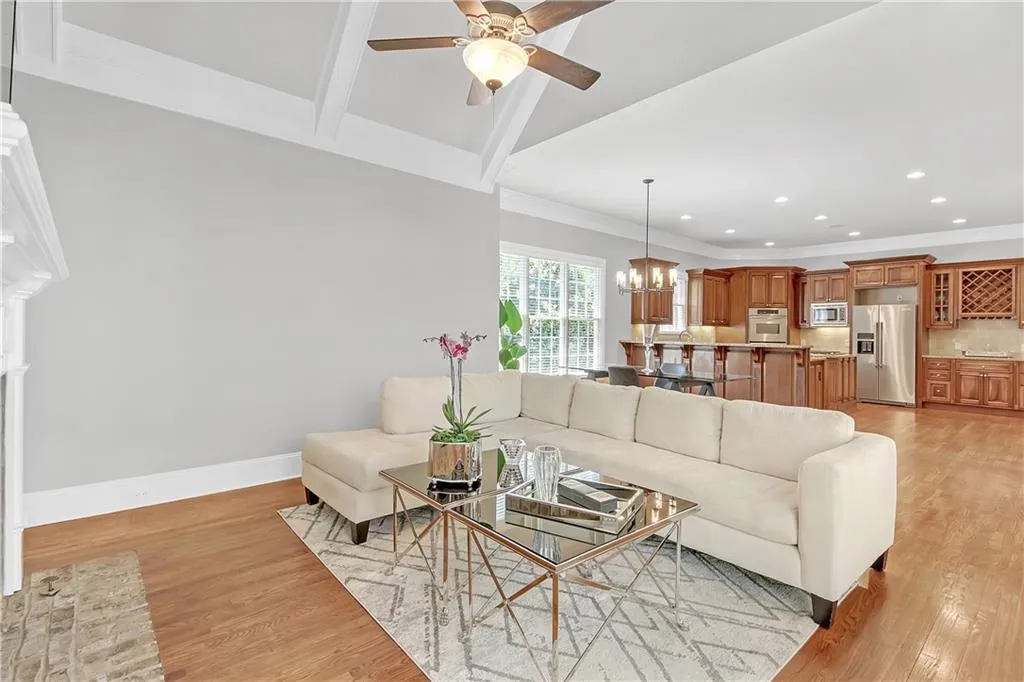 Living room featuring vaulted ceiling with beams, ornamental molding, light wood-type flooring, and ceiling fan with notable chandelier