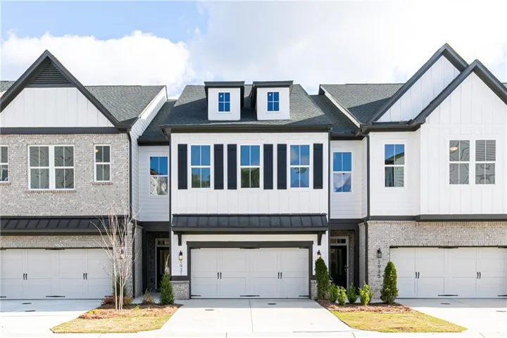 Modern townhome exterior featuring white board-and-batten siding, light gray brick accents, dark gray shingle roofing, and black window shutters