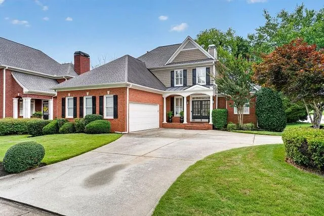 Brick and shingle exterior featuring a columned entry, covered porch, and a two-car garage with an automatic door