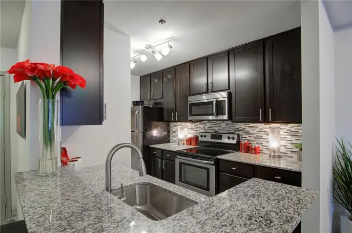Kitchen featuring stainless steel appliances, light stone counters, dark brown cabinetry, and tasteful backsplash