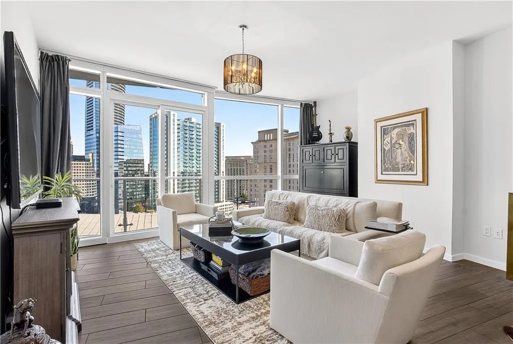 Living area with floor to ceiling windows, dark wood-style flooring, suspended lighting, and a city view