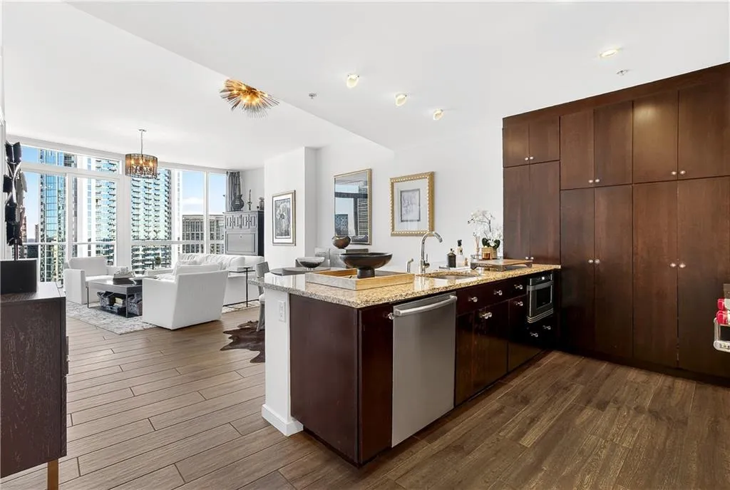 Kitchen with a peninsula, dark wood-style flooring, light stone counters, stainless steel dishwasher, and dark wood finish cabinetry