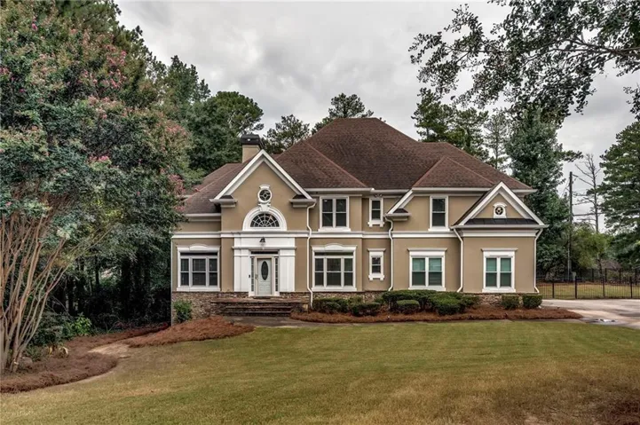 Stucco exterior with stone accents, mature trees, a manicured lawn, and multi-pane windows