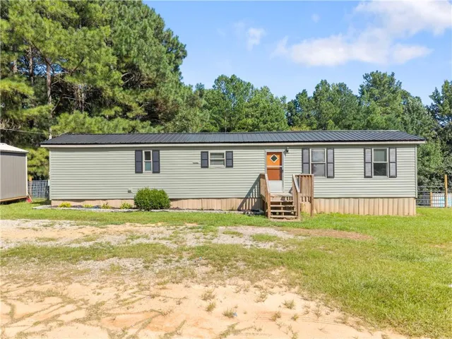 Light green horizontal siding exterior with a dark metal roof, featuring a wooden entry deck and steps