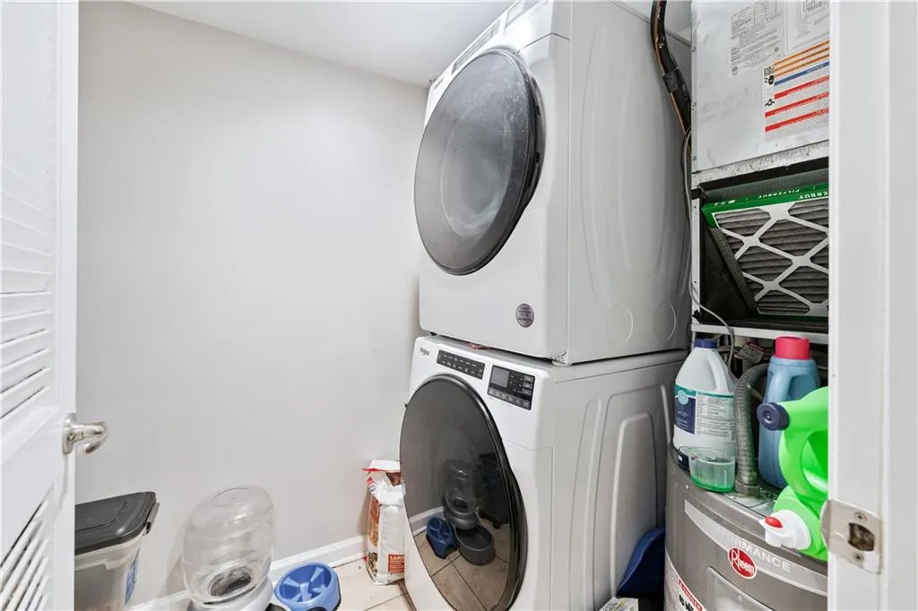 Laundry area featuring stacked washing machine and dryer, tile patterned flooring, water heater, and heating unit