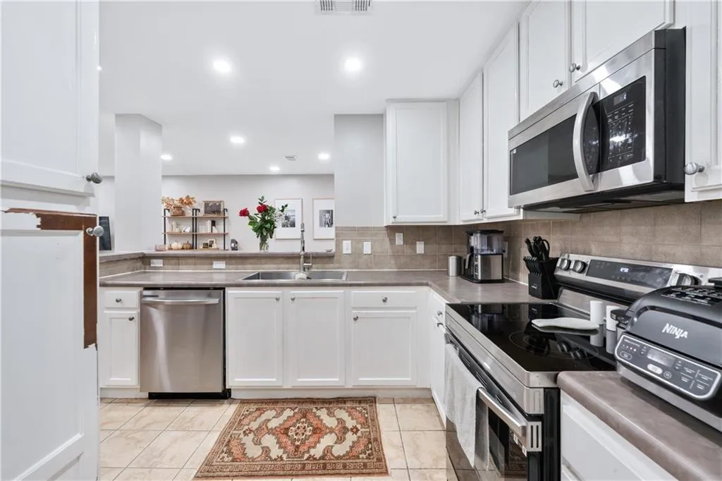 Kitchen with stainless steel appliances, white cabinets, decorative backsplash, light tile patterned floors, and recessed lighting