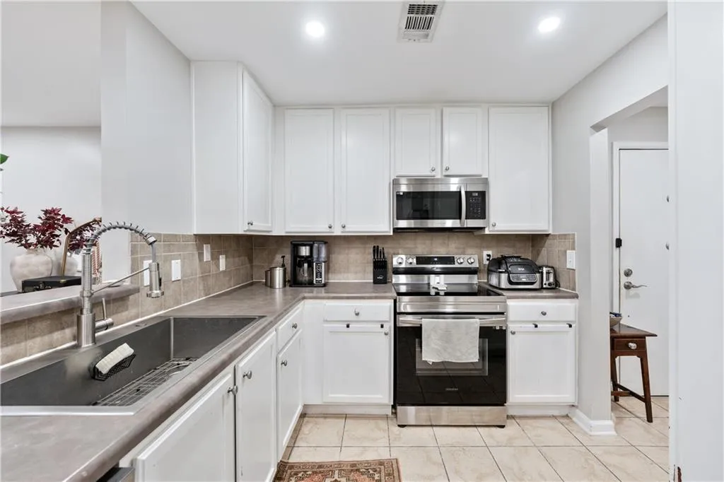 Kitchen featuring tasteful backsplash, appliances with stainless steel finishes, white cabinets, light tile patterned floors, and recessed lighting