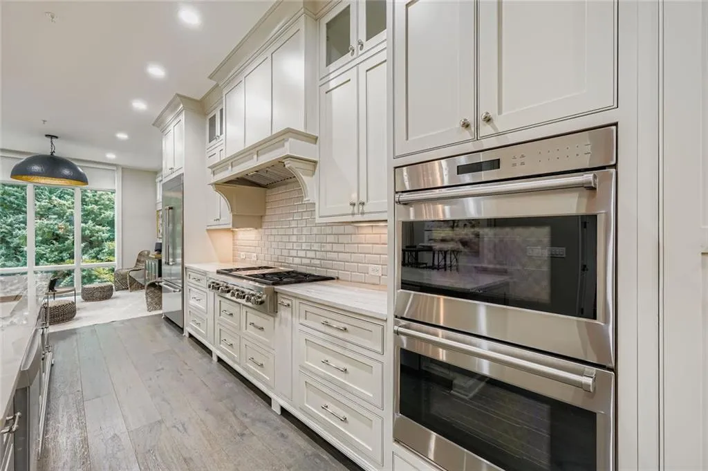 Kitchen featuring high end appliances with stainless steel finishes, tasteful backsplash, recessed lighting, white cabinets, and light wood-type flooring