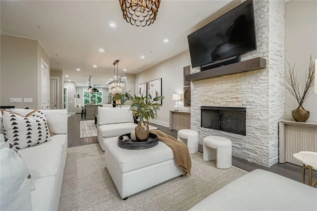 Living room with wood finished floors, a chandelier, a stone fireplace, recessed lighting, and crown molding