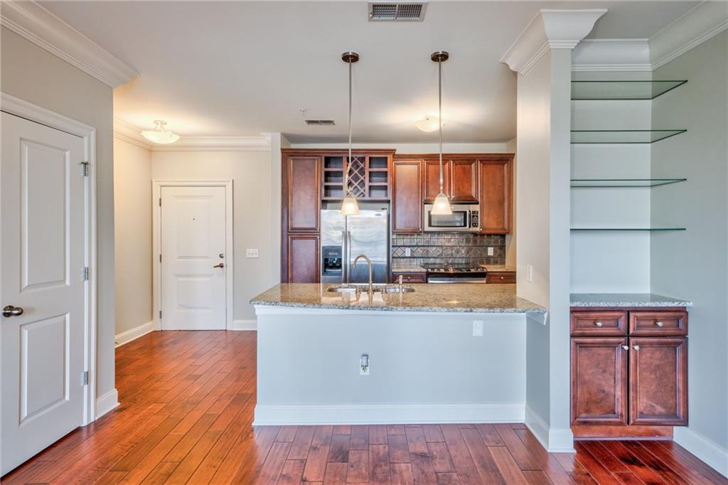 Kitchen featuring stainless steel appliances, light stone counters, backsplash, sink, and dark wood-type flooring