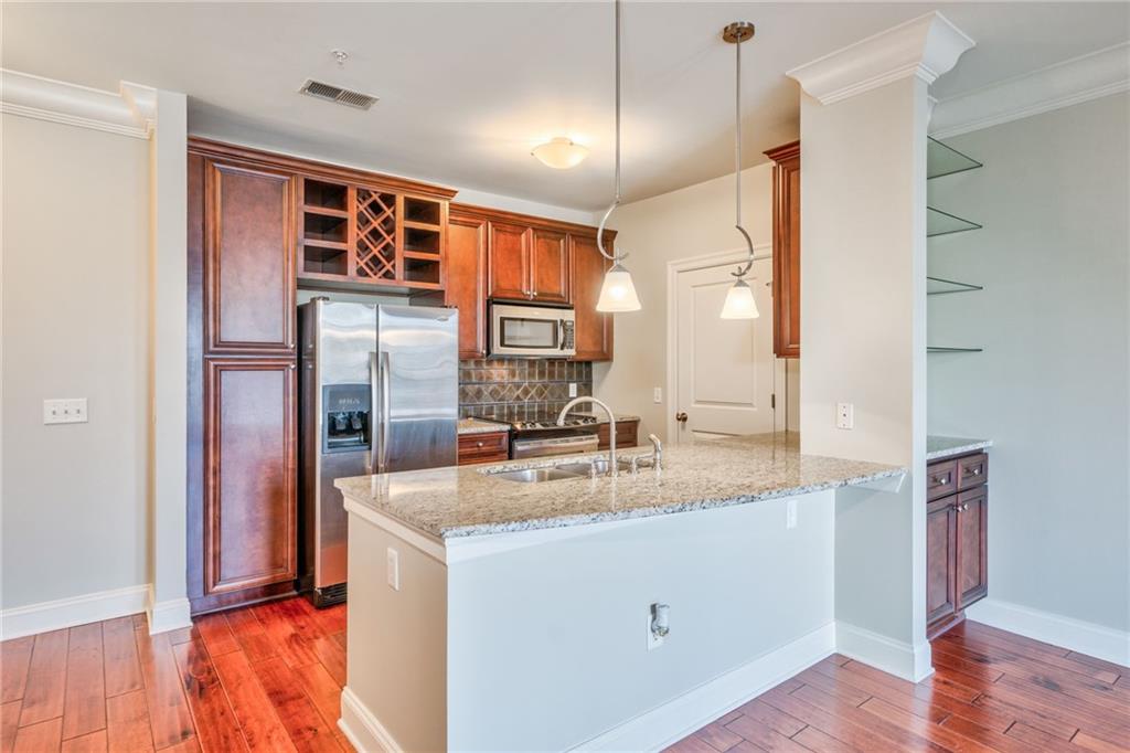 Kitchen with pendant lighting, hardwood / wood-style floors, light stone countertops, and appliances with stainless steel finishes
