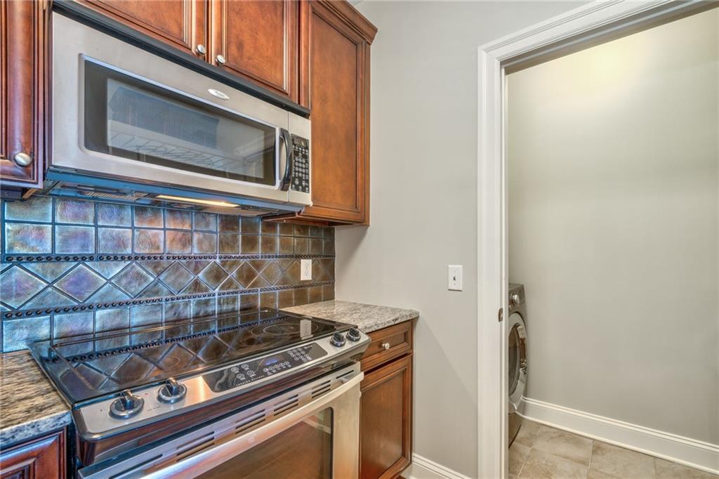 Kitchen with washer / dryer, appliances with stainless steel finishes, stone counters, light tile floors, and backsplash