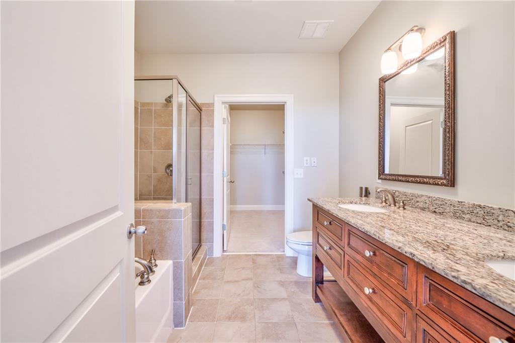Full bathroom featuring oversized vanity, toilet, dual sinks, shower with separate bathtub, and tile floors