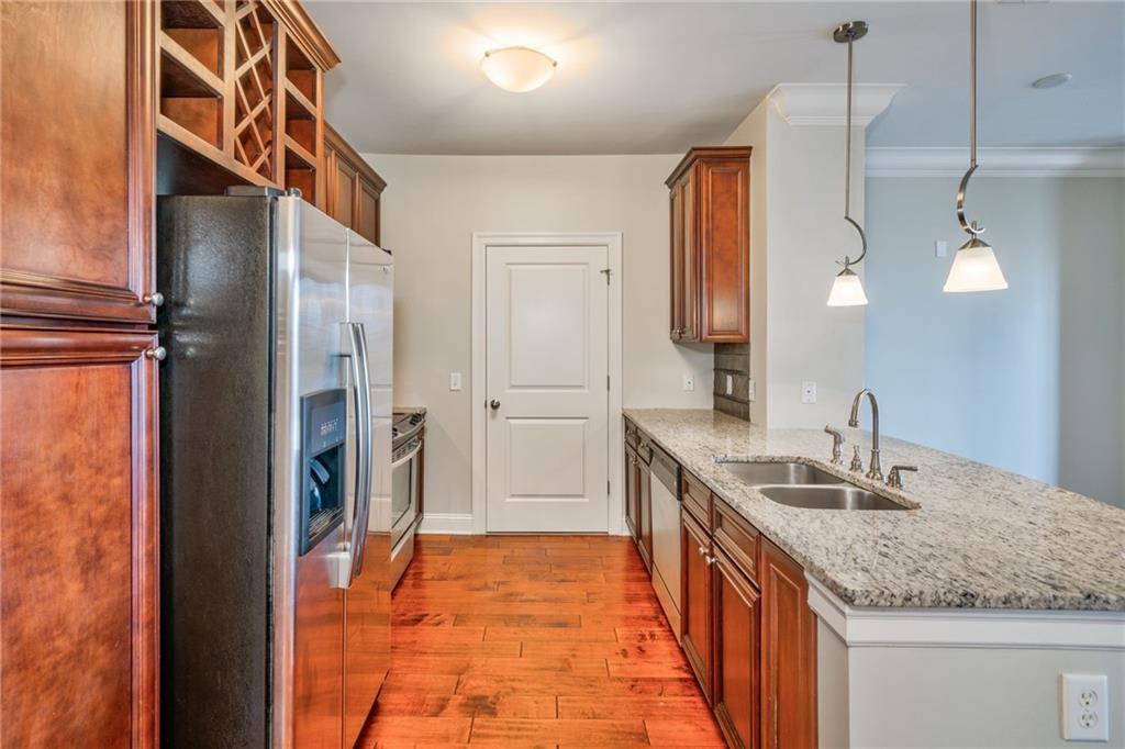 Kitchen featuring light wood-type flooring, light stone countertops, decorative light fixtures, sink, and stainless steel appliances