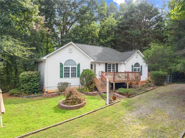 White siding exterior with green shutters, elevated deck with natural wood railing, gravel driveway, and a manicured lawn