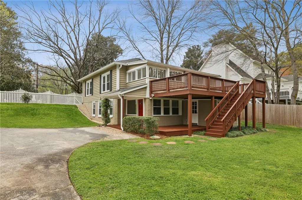 Back of property with a wooden deck, driveway, and parking
