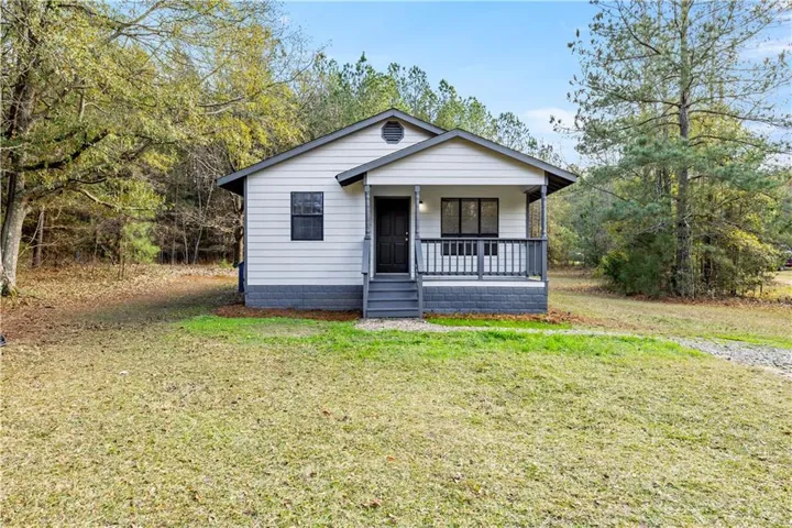 White siding exterior with a dark gray brick foundation, dark gray trim, and a covered porch featuring a dark gray railing