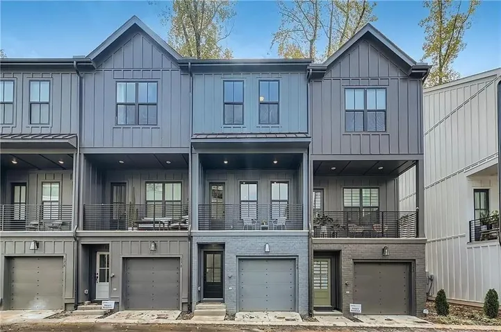 Modern multi-level townhome architecture featuring board and batten siding, brick accents, multiple balconies with metal railings, and integrated single-car garages