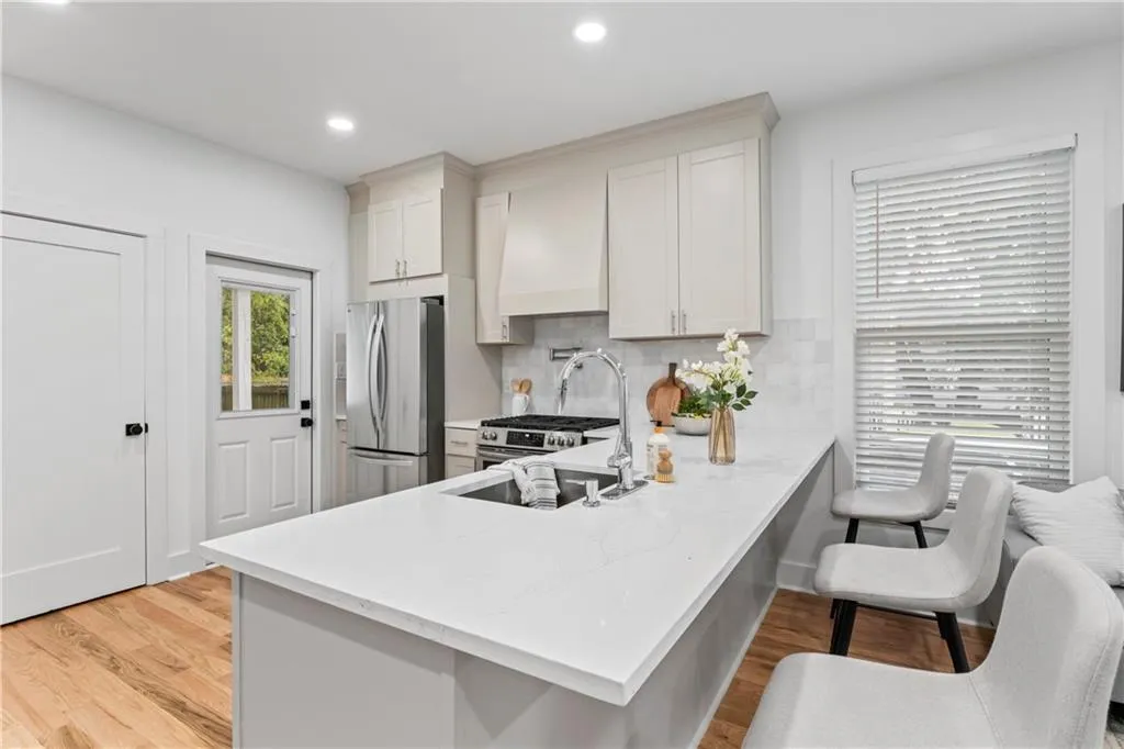 Kitchen with appliances with stainless steel finishes, light wood finished floors, light stone countertops, backsplash, and recessed lighting