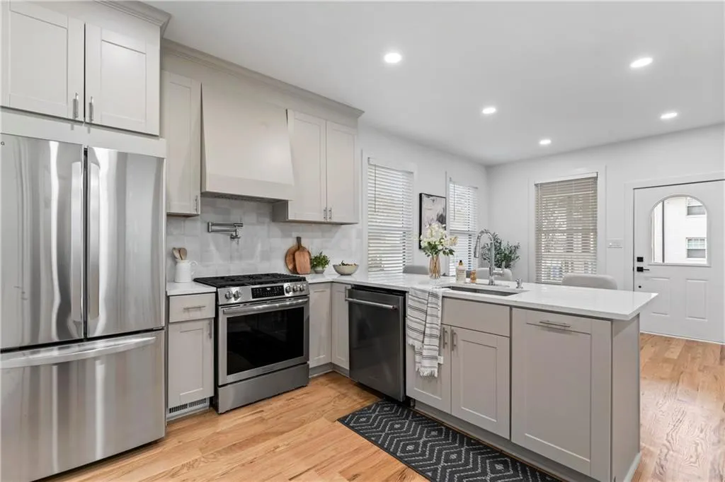 Kitchen featuring stainless steel appliances, decorative backsplash, a peninsula, light wood-style floors, and plenty of natural light