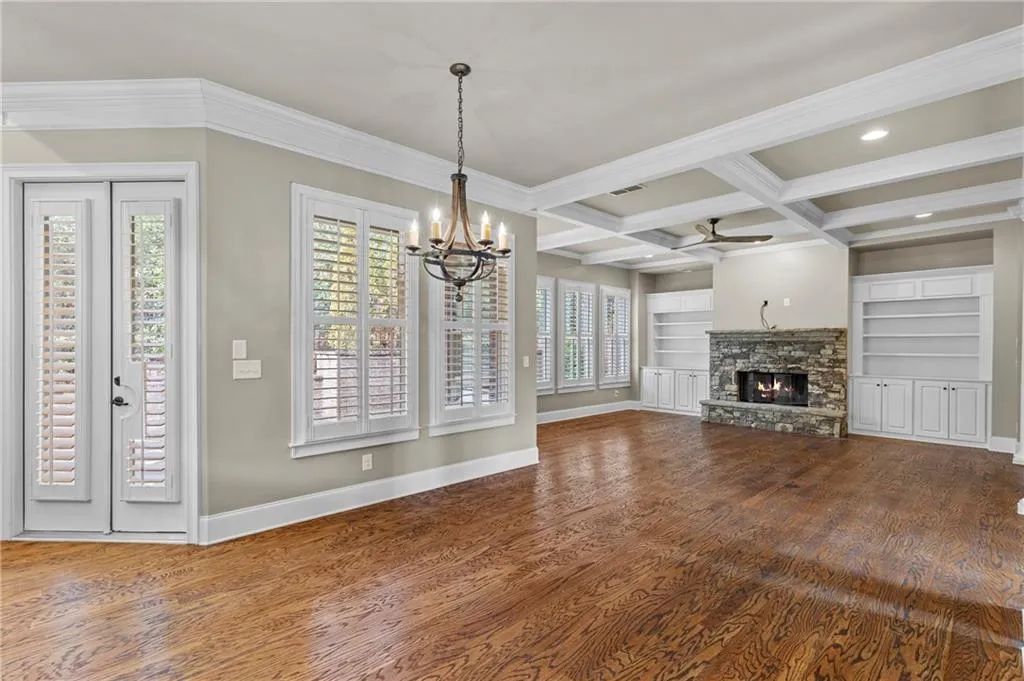 Unfurnished living room featuring coffered ceiling, a stone fireplace, built in shelves, beam ceiling, and a chandelier