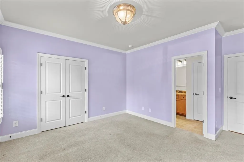 Unfurnished bedroom featuring ornamental molding, light carpet, a closet, and ensuite bath