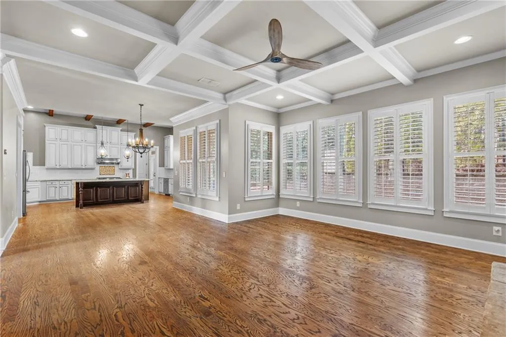Unfurnished living room with a chandelier, coffered ceiling, beamed ceiling, crown molding, and dark wood-type flooring