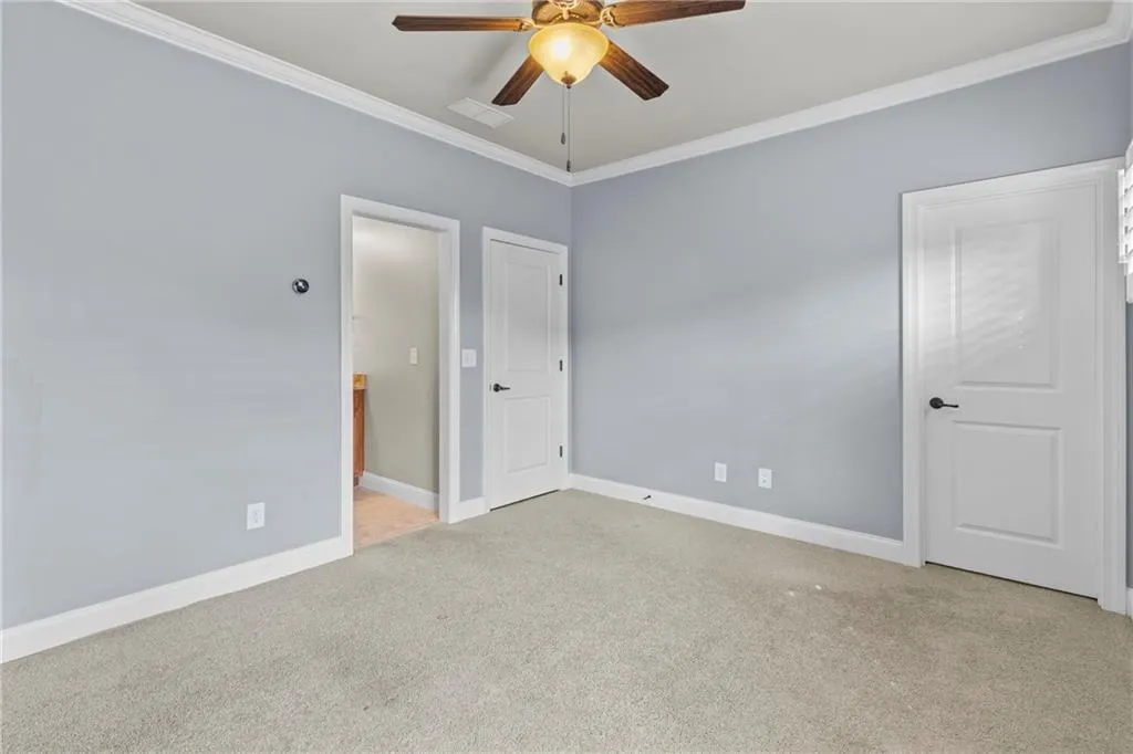 Unfurnished bedroom featuring light colored carpet, crown molding, a ceiling fan, and ensuite bathroom