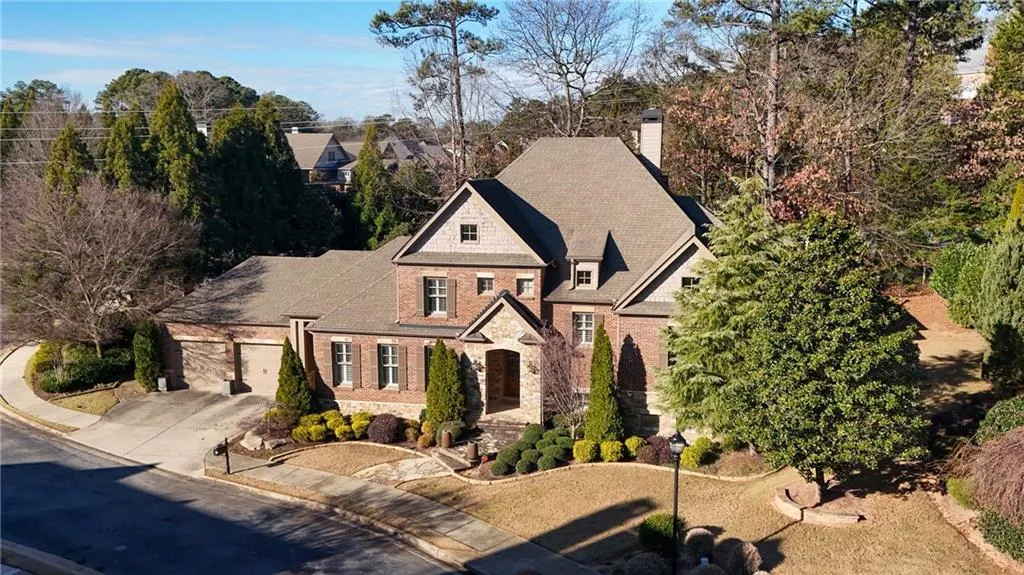 View of front of property featuring stone siding, concrete driveway, a chimney, view of wooded area, and a garage