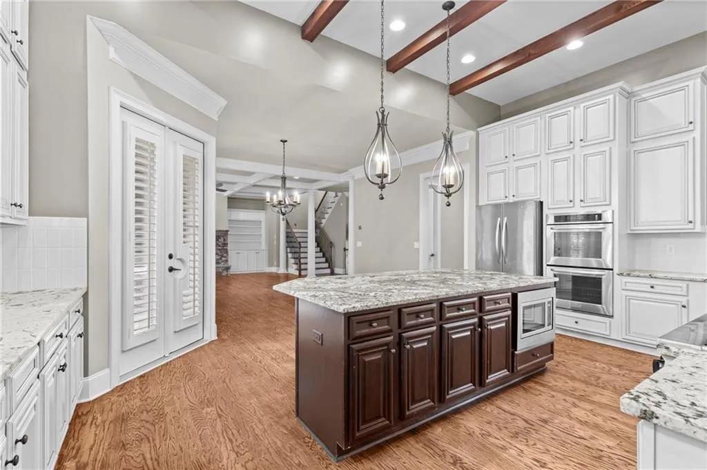Kitchen featuring tasteful backsplash, beam ceiling, white cabinetry, light stone counters, and ornamental molding
