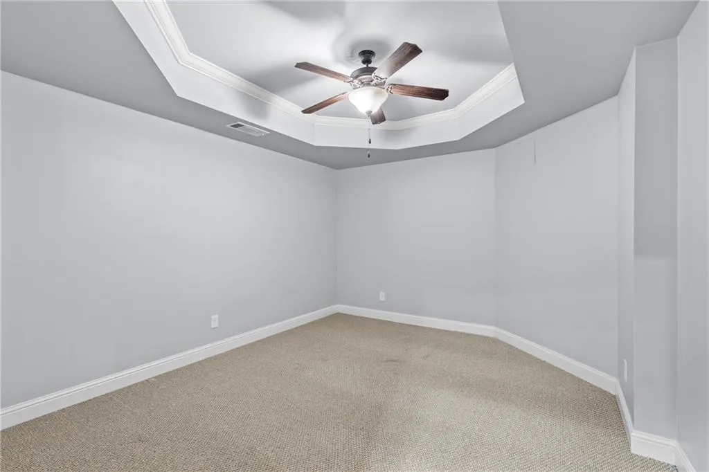 Carpeted spare room with a tray ceiling, ornamental molding, and a ceiling fan