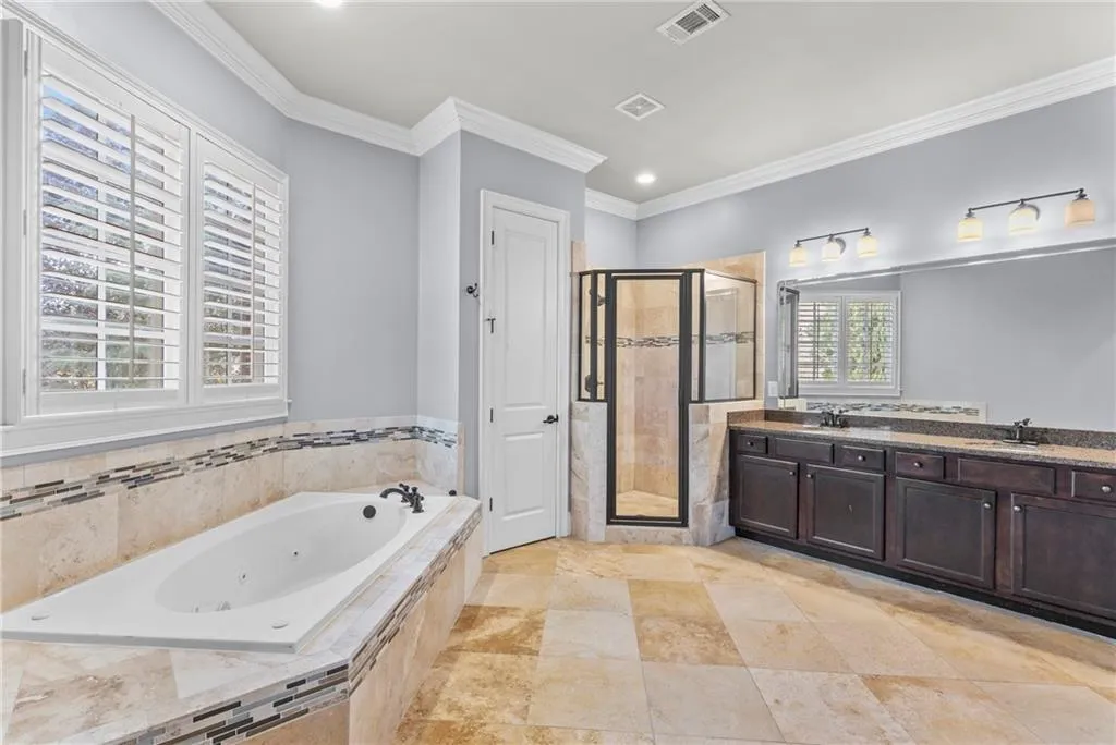 Full bathroom featuring a tub with jets, double vanity, a stall shower, crown molding, and recessed lighting