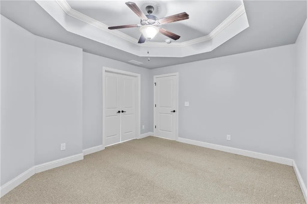 Unfurnished bedroom featuring a tray ceiling, crown molding, carpet flooring, a closet, and ceiling fan