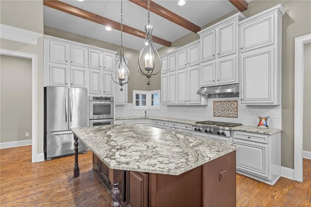 Kitchen with stainless steel appliances, light stone countertops, decorative light fixtures, a kitchen island, and tasteful backsplash