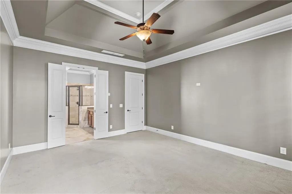 Unfurnished bedroom with crown molding, a ceiling fan, a raised ceiling, and ensuite bath