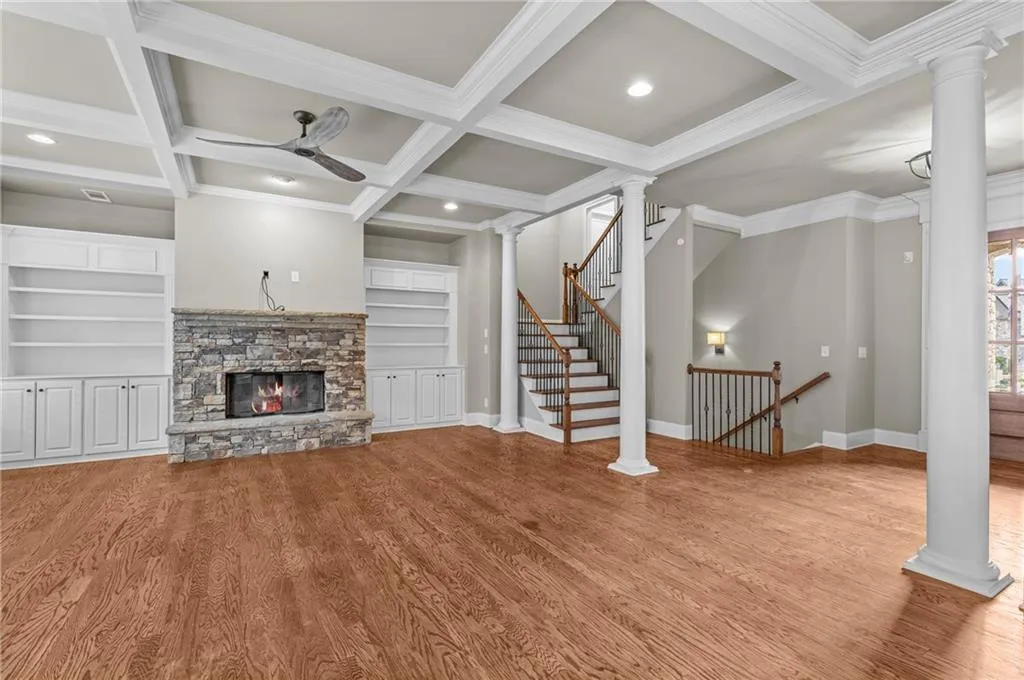 Unfurnished living room with ornate columns, coffered ceiling, beamed ceiling, light wood-style floors, and a stone fireplace